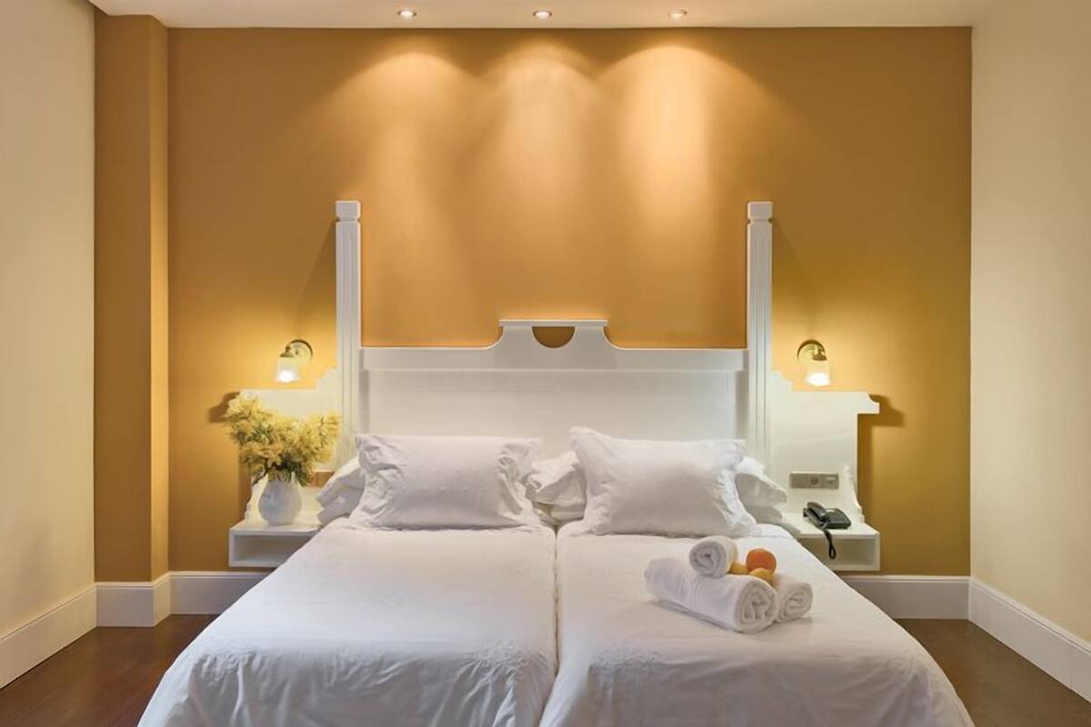 Un lit double avec du linge de lit blanc, deux tables de chevet avec des lampes et un vase de fleurs.