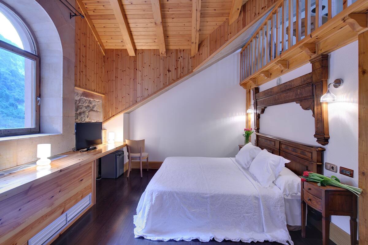 Une chambre avec un plafond en bois, un lit, un bureau, une chaise et une fenêtre.
