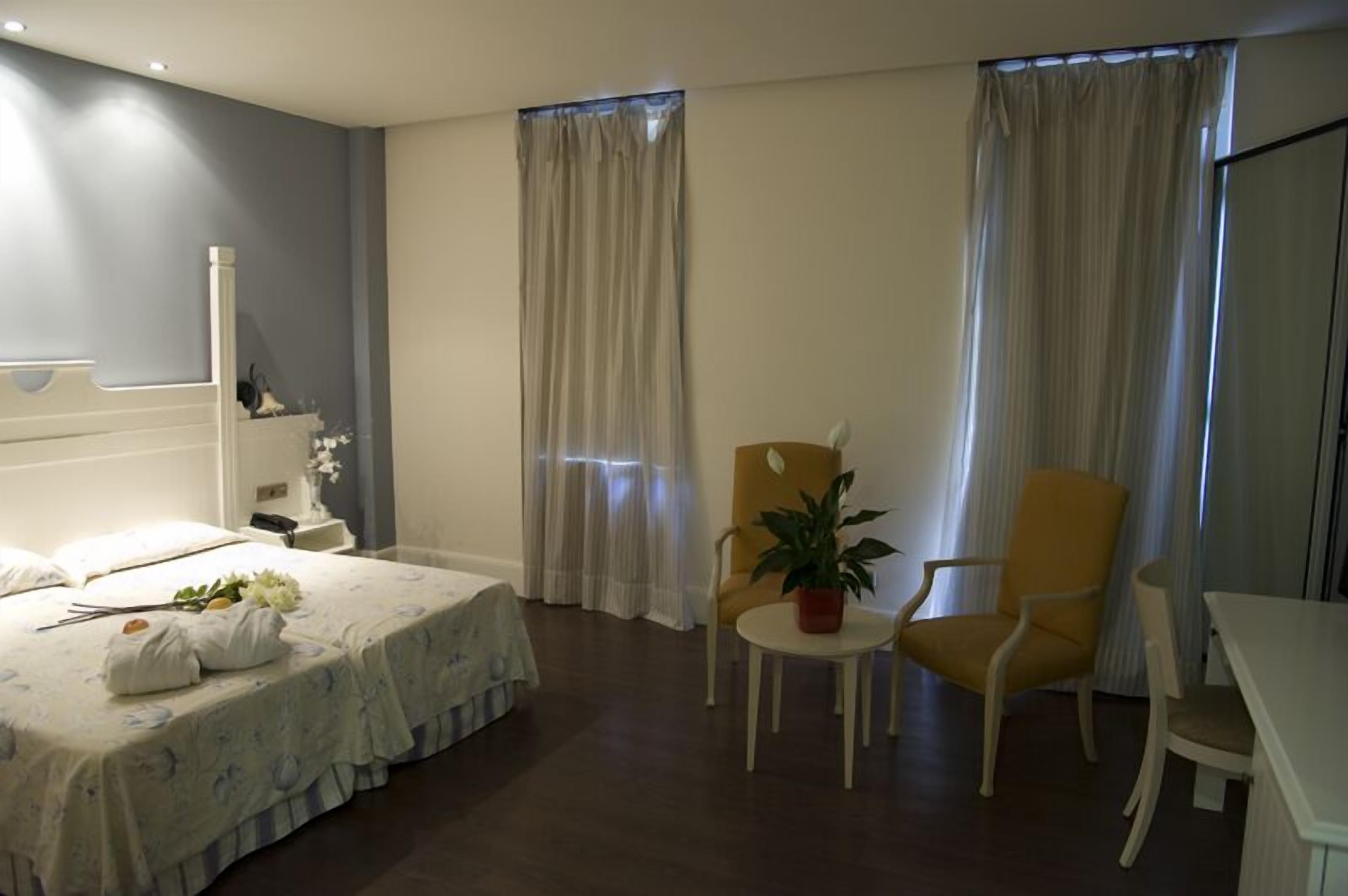 A hotel room with a bed, a small table with a plant, two chairs, and a desk.