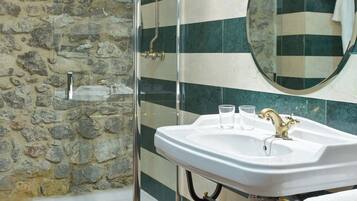 Een badkamer met een douchecabine van glas, een wit wastafelmeubel met gouden details en een spiegel met een handdoek op een rek.