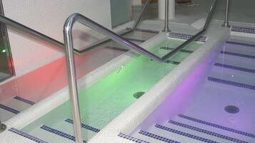 A multi-level indoor swimming pool with glass railings and tiled floors.