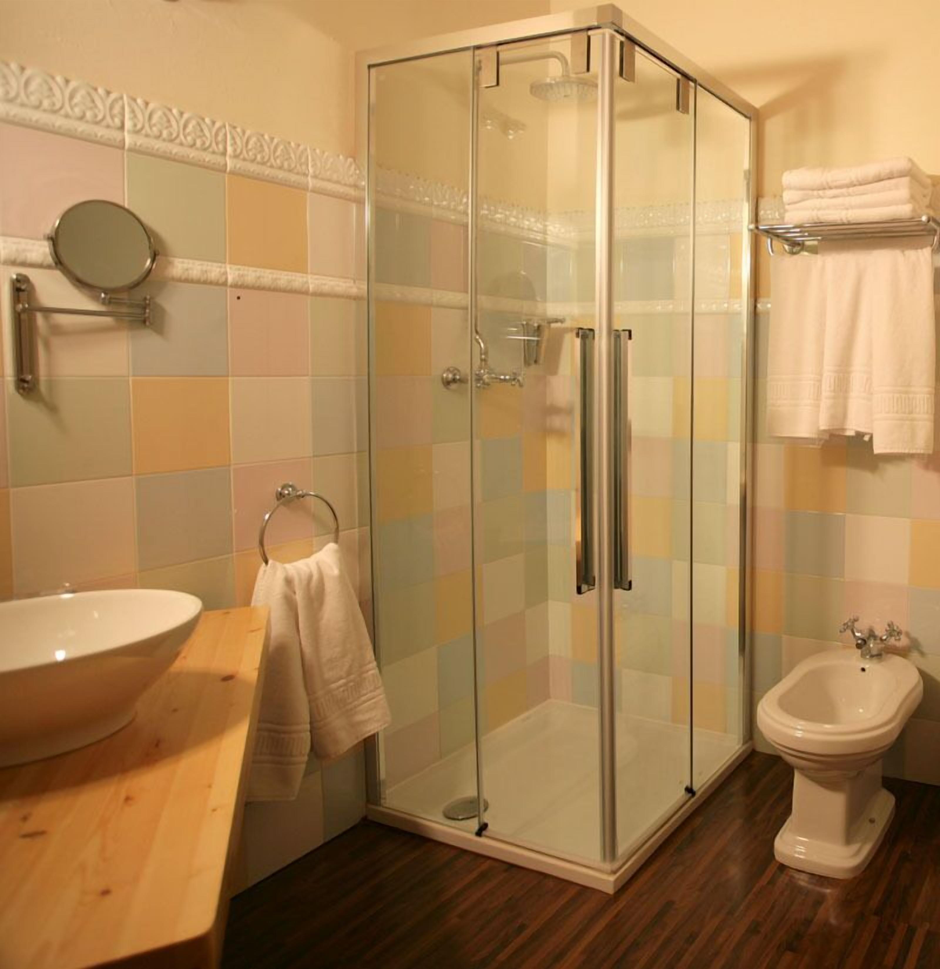 Ein Badezimmer mit Duschkabine aus Glas, einem Holzkosmetikschrank mit Waschbecken, einem Bidet und einem Spiegel an der Wand.