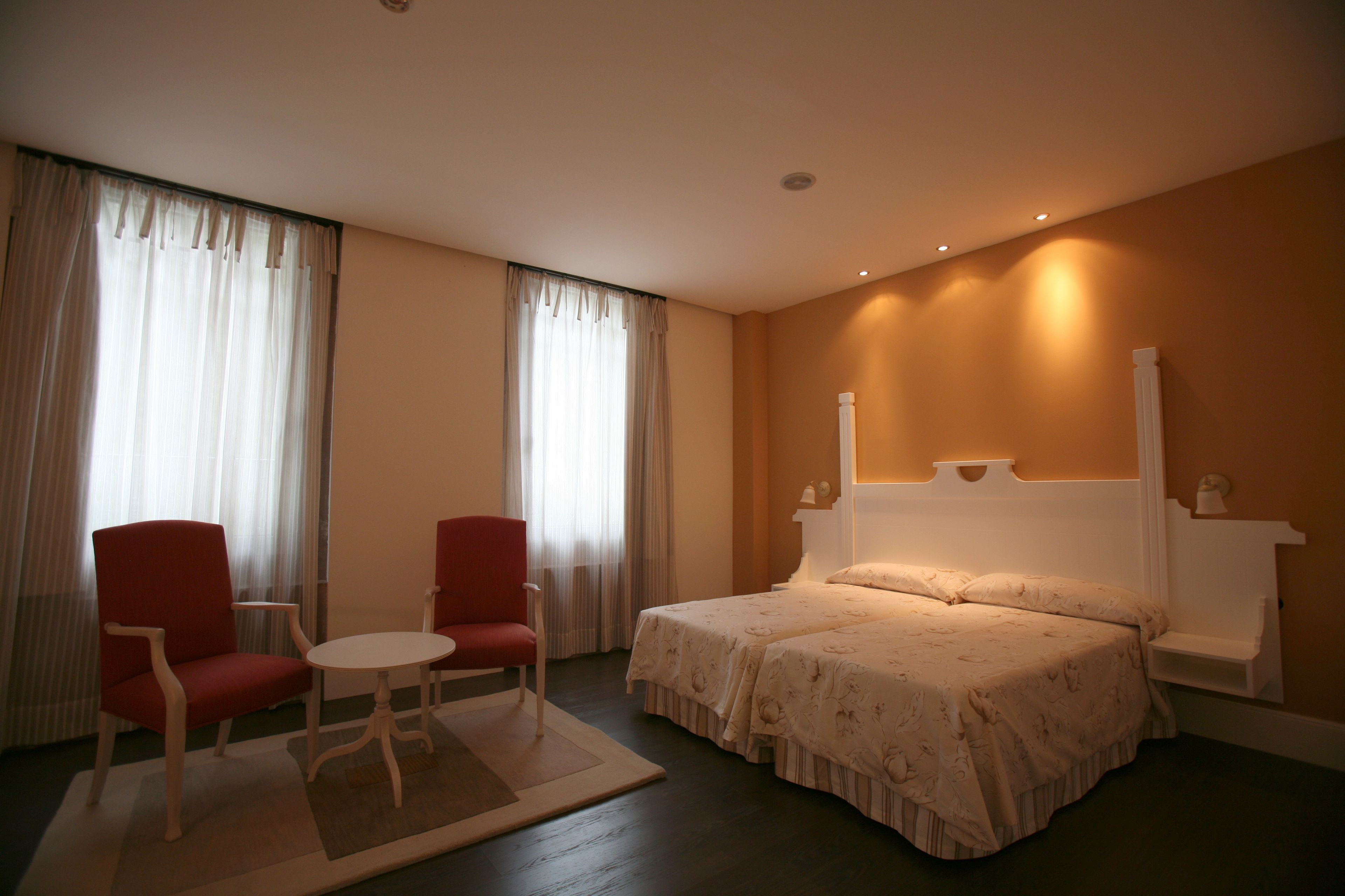 Habitación de hotel con cama, dos sillas, una mesita y ventana con cortinas.