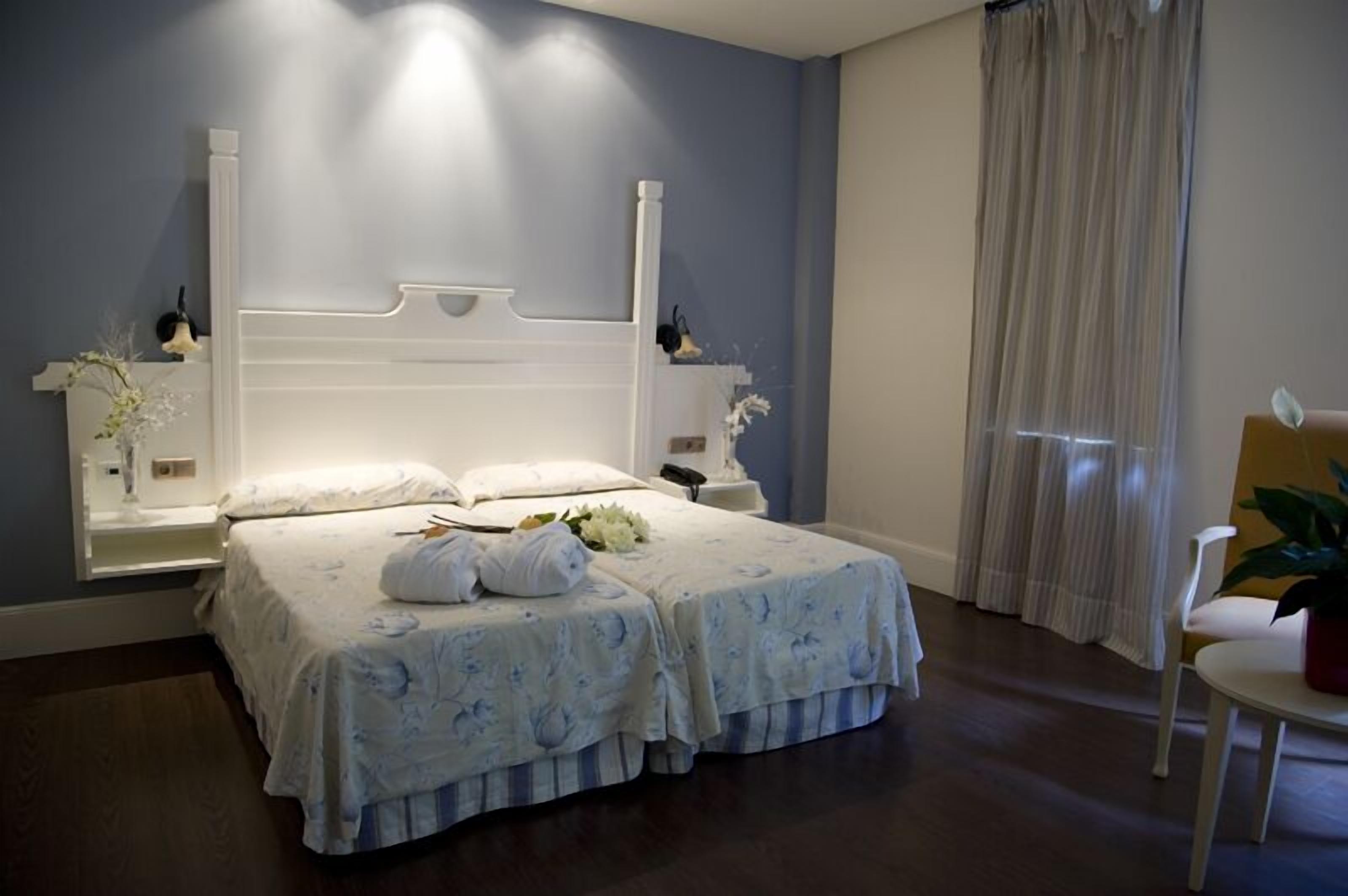 Un dormitorio con una cama grande, mesitas de noche, una silla y una ventana con cortinas.