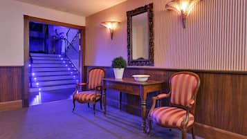 A hallway with a staircase, striped wallpaper, a large mirror, and two wall-mounted lamps.