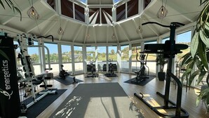 Un gimnasio amplio con diferentes equipos de ejercicio, ventanas grandes y un techo alto.