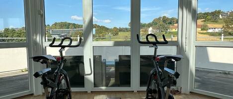 Ein Indoor-Cycling-Bereich mit zwei Ergometer, großen Fenstern und Blick auf die Landschaft.