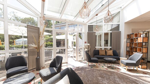 Un luminoso solario amplio con muebles modernos, ventanas grandes y una estantería.