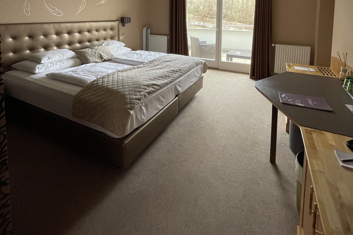 A bedroom with a large bed, a wooden desk, and a view of the outdoors through a sliding glass door.