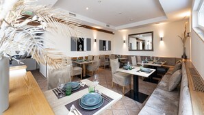 Un comedor moderno con mesas preparadas para dos, que ofrece una variedad de opciones de asientos, incluyendo sillas y un sofá.