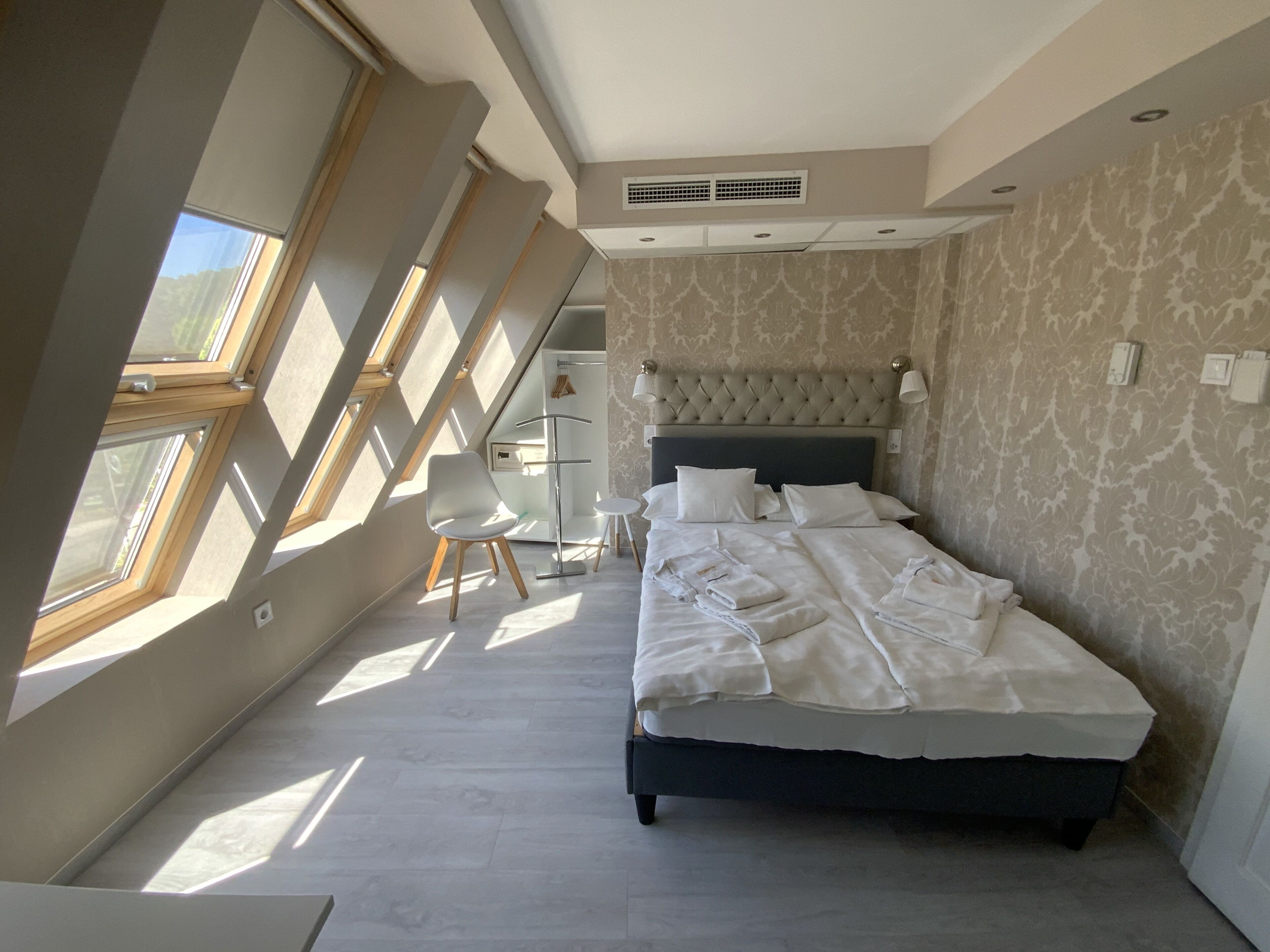 Ein Schlafzimmer mit einem großen Bett, einem Sessel und einem Schreibtisch. Es gibt Dachfenster und eine Wand mit Muster.