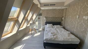 Ein Schlafzimmer mit einem großen Bett, einem Sessel und einem Schreibtisch. Es gibt Dachfenster und eine Wand mit Muster.