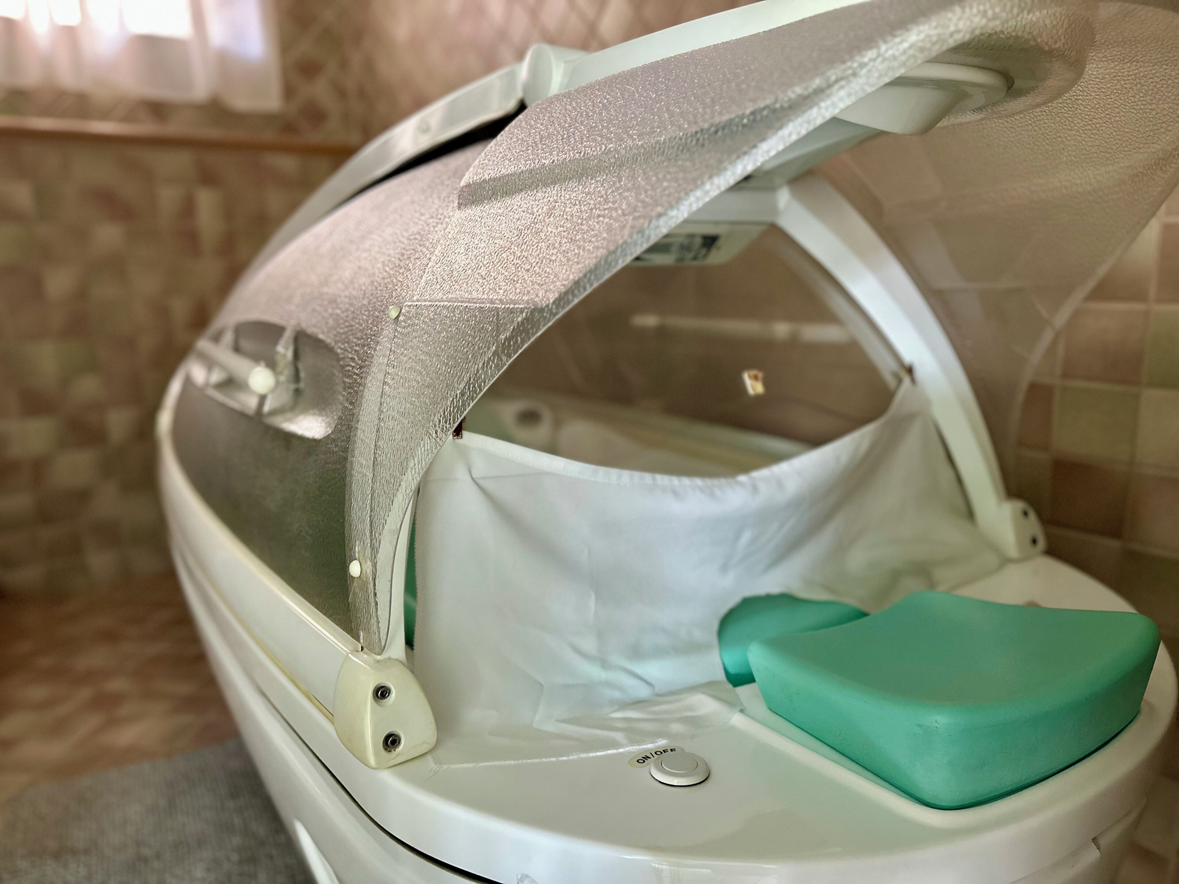 Een draagbaar toilet met een scharnierend deksel, een groene schoonmaakborstel en een witte plastic zitting.