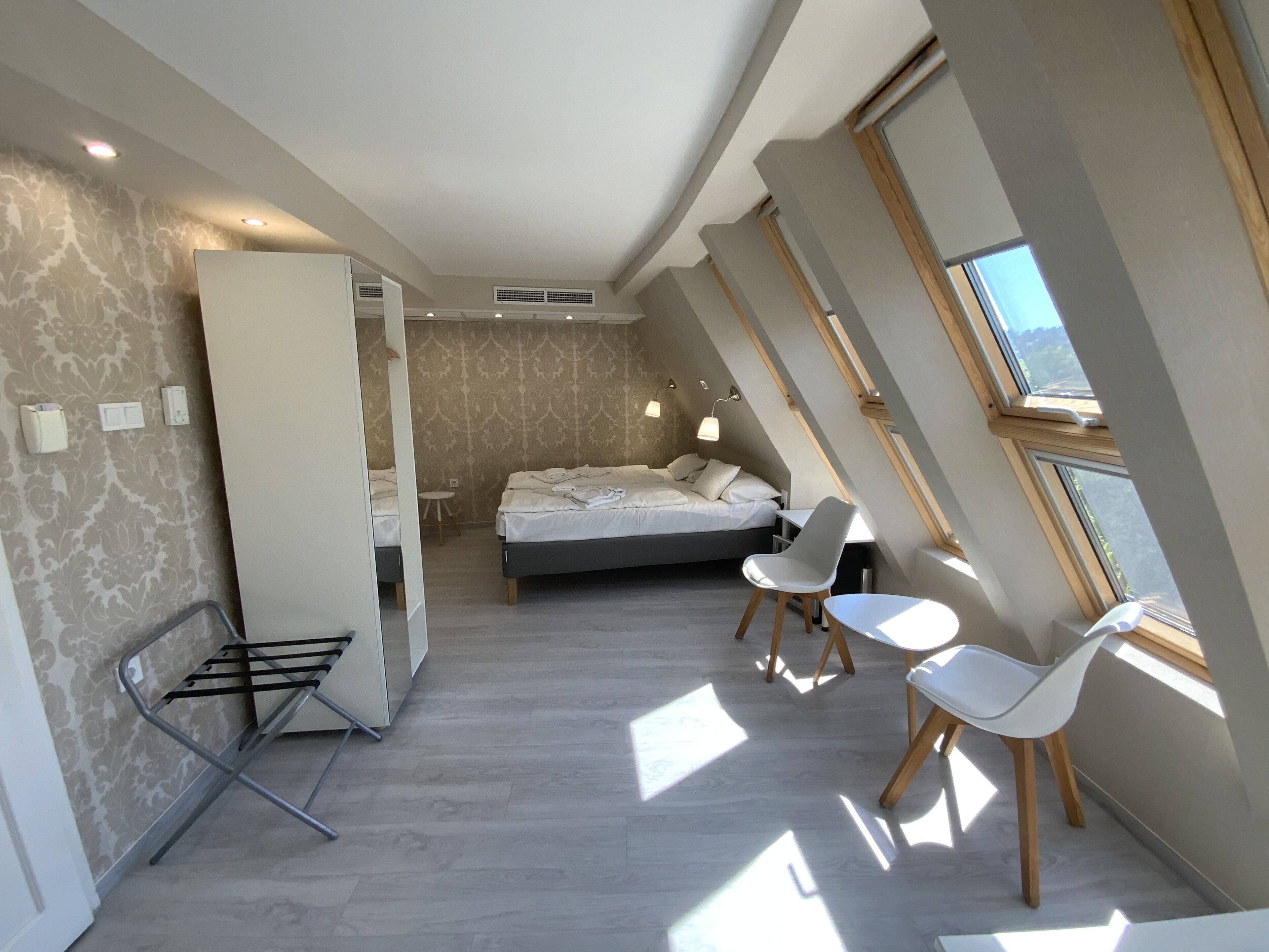 Un dormitorio moderno con una cama, dos sillas blancas, una mesita y un tragaluz.