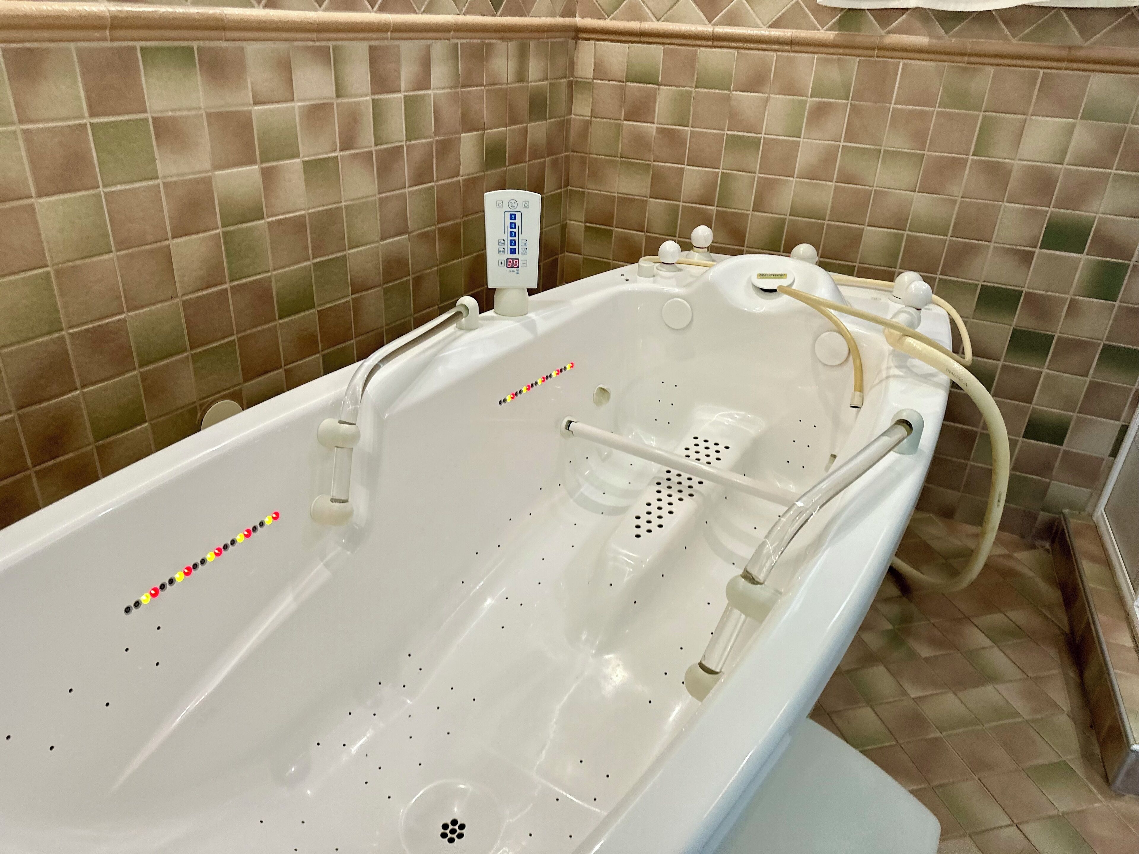 A white bathtub with a control panel, a handheld showerhead, and a handheld massager.