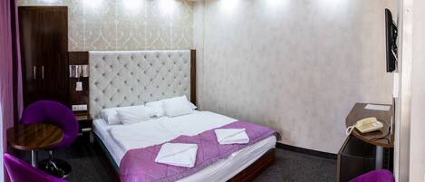 A hotel room with a large bed, two purple chairs, a small table, and a telephone.