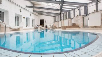 An indoor swimming pool with clear blue water, surrounded by tiled walls and a high ceiling with metal beams.