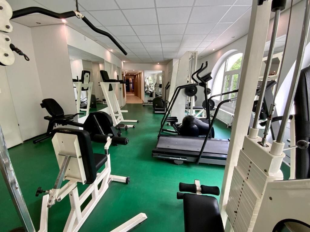 A gym with various exercise machines, a green floor, and a mirrored wall.