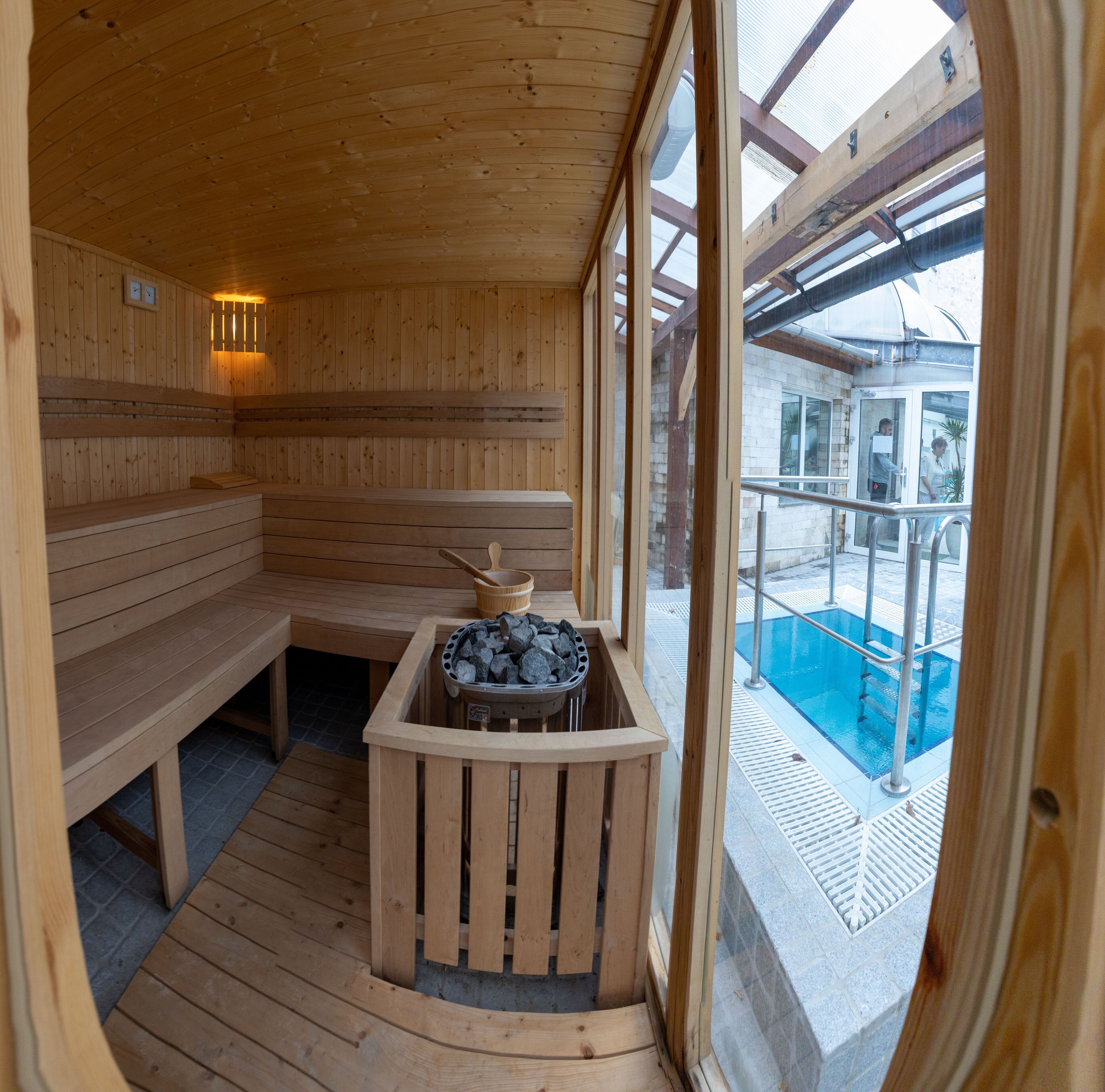 Una sauna de madera con bancos y una camilla, con ventana que da a una zona de piscina.