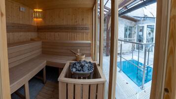 Una sauna de madera con bancos y una camilla, con ventana que da a una zona de piscina.