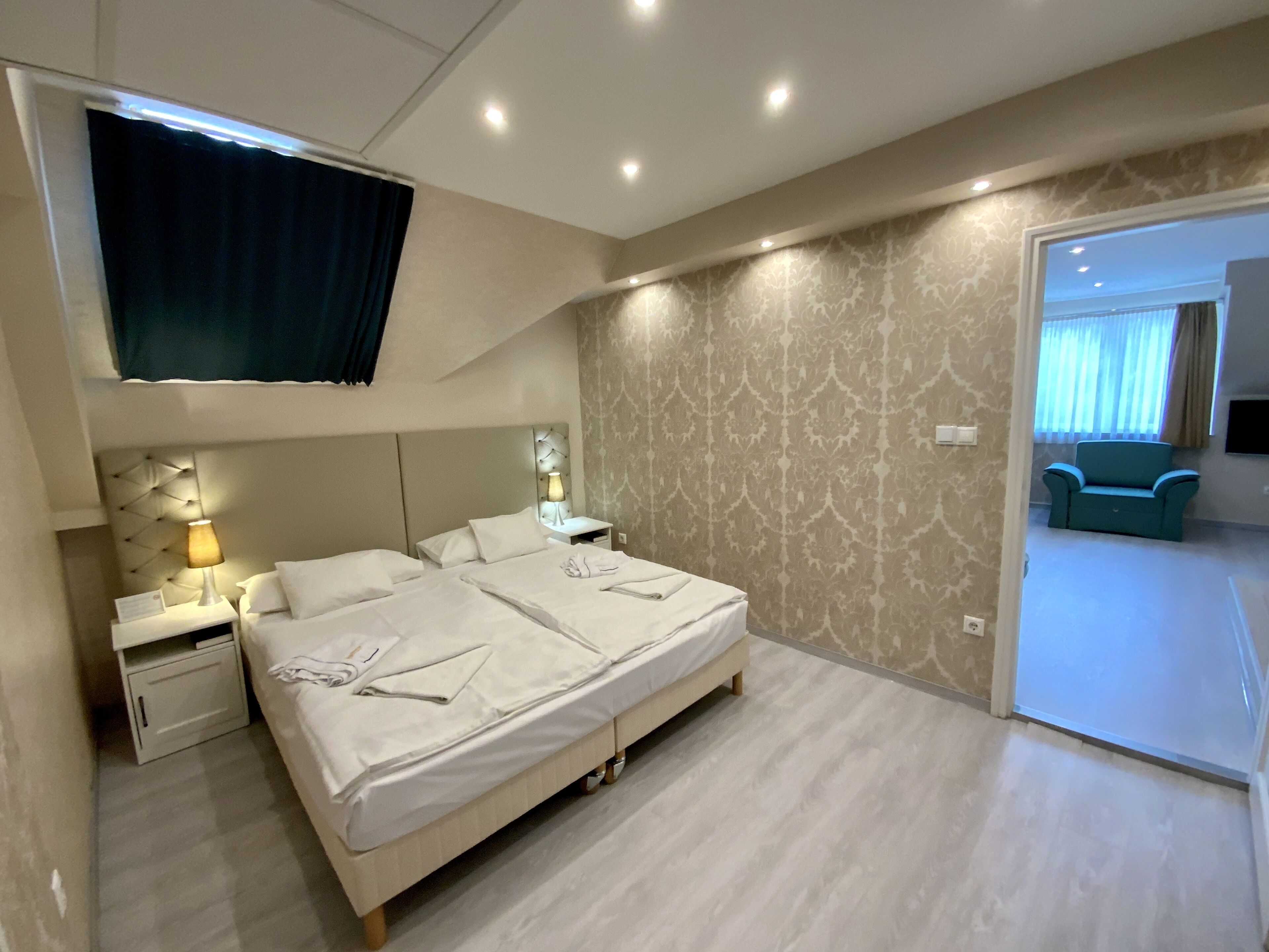 A modern hotel room with a large bed, bedside tables with lamps, a TV mounted on the wall, and a patterned wallpaper.