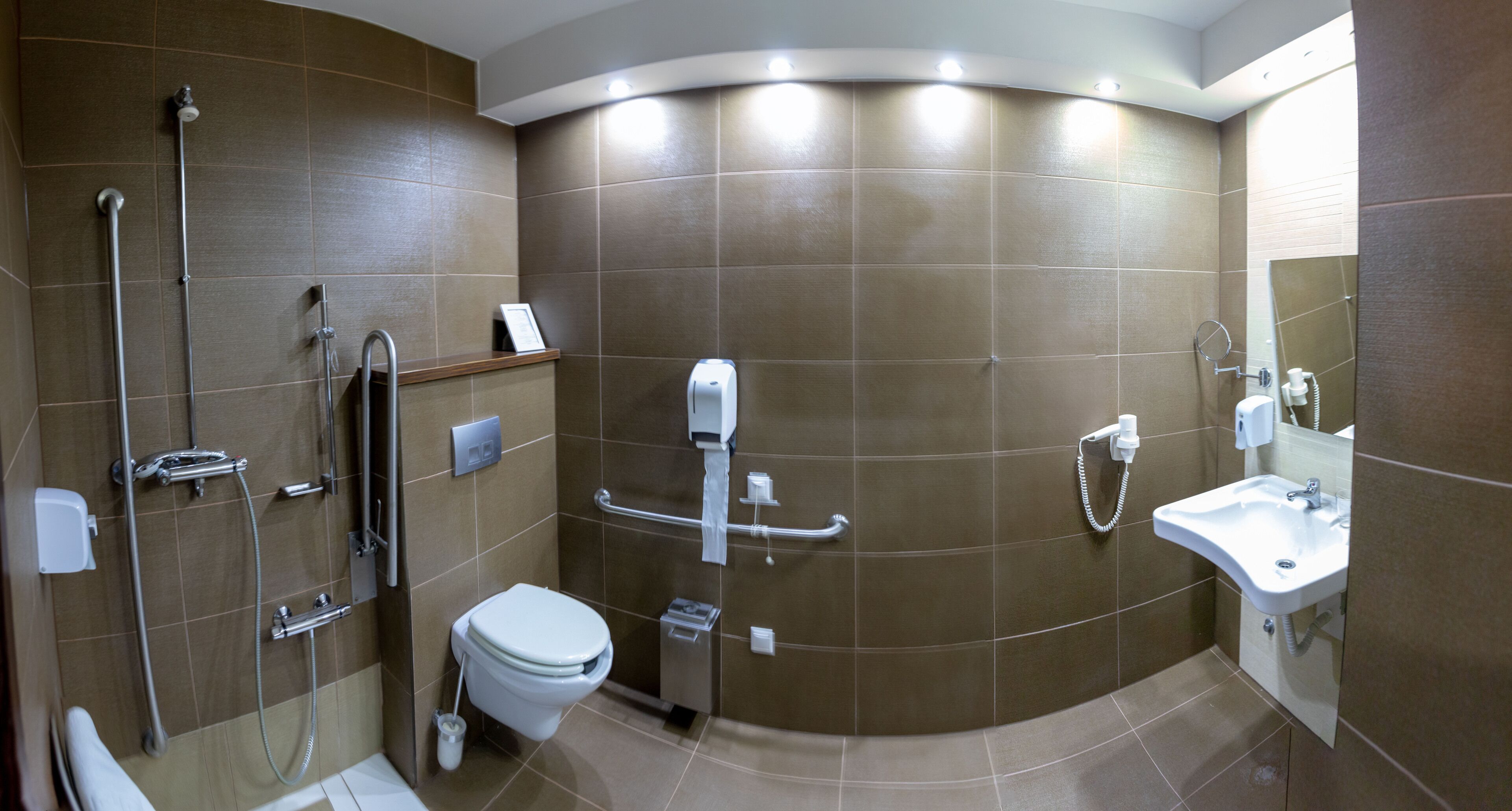 Un baño moderno con ducha curva, inodoro, lavamanos y secamanos.