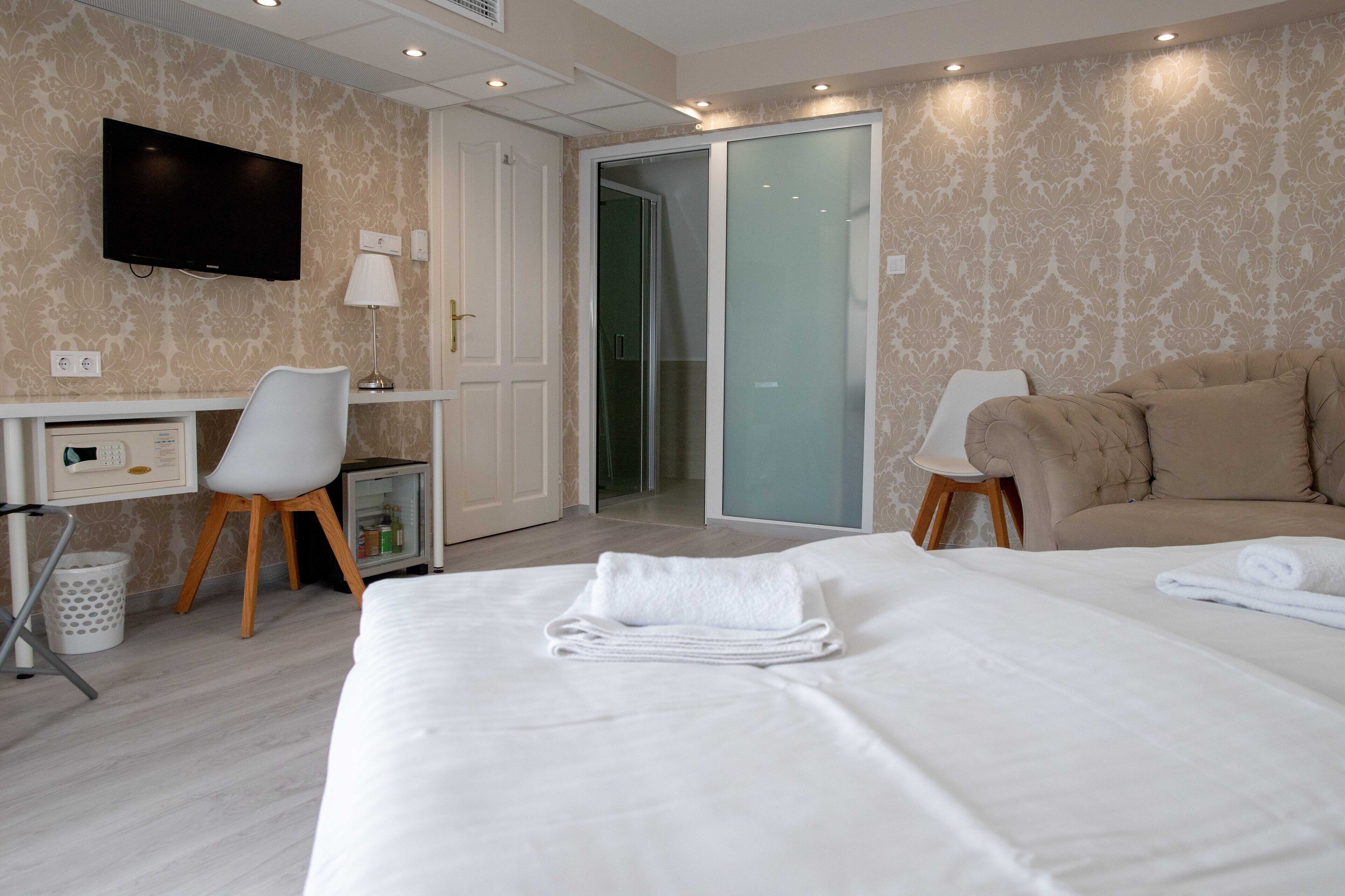A hotel room with a bed, a desk, a chair, a TV, and a sliding door to a shower area.