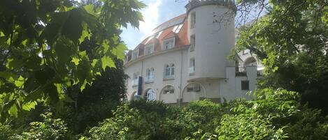 A historic building with a round tower and arched windows, surrounded by lush greenery.