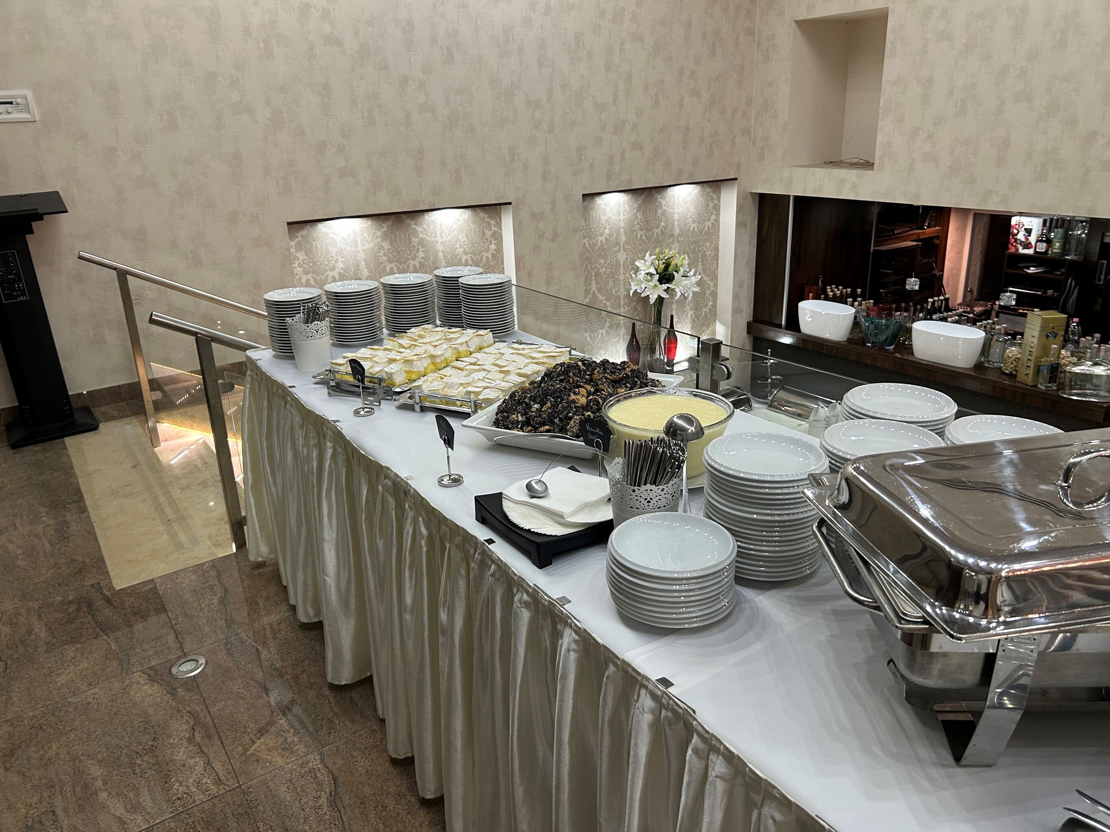 Montaje de bufé con diversos alimentos y utensilios, una baranda de vidrio y un piso de baldosas.