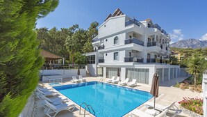 A multi-story hotel with a swimming pool, sun loungers, and a mountain backdrop. - Forest Park Hotel (Kemer)