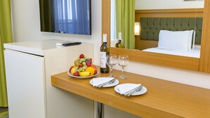 A hotel room with a bed, a TV mounted on the wall, a small desk with a fruit bowl, wine glasses, and a bottle of wine. - Forest Park Hotel (Kemer)