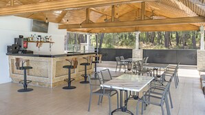 An outdoor patio area with a bar, seating, and a view of the forest. - Forest Park Hotel (Kemer)
