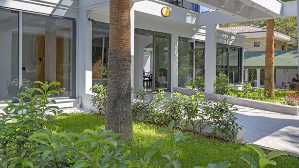 A modern building with large glass windows, a covered outdoor area, and a clock. - Forest Park Hotel (Kemer)