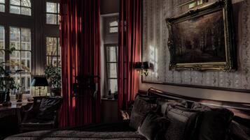 A room with a large bed, a desk with a lamp, a chair, and a large window with curtains.