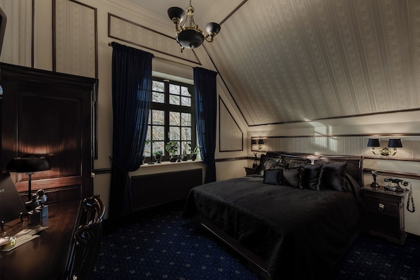Una habitación con una cama grande, un escritorio con lámpara, una ventana con cortinas y un candelabro.