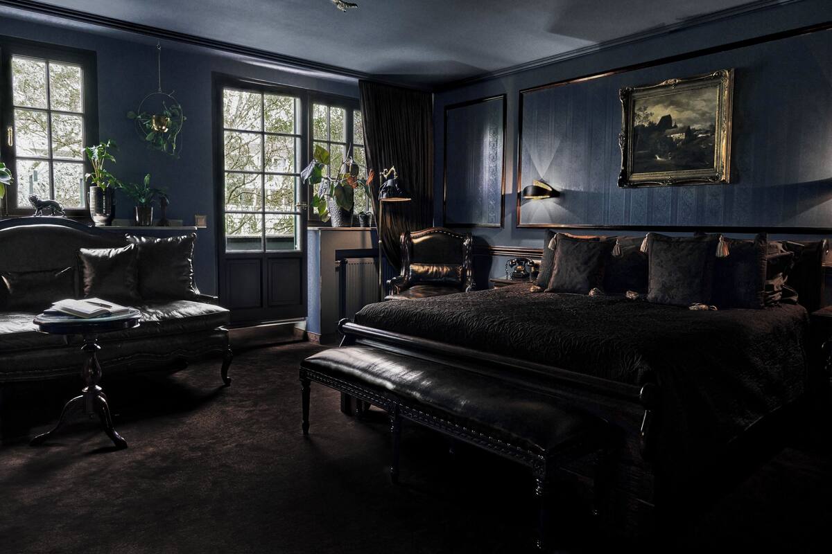 A dark-themed bedroom with a large bed, a chaise lounge, and a vintage telephone.
