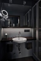 Un bagno moderno con lavandino bianco, uno specchio con luce ad anello e box doccia in vetro.