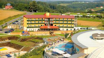 A multi-story hotel with a swimming pool, outdoor seating, and a view of the surrounding countryside.
