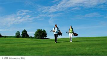 Golfers walk along the well-manicured fairway, surrounded by trees.