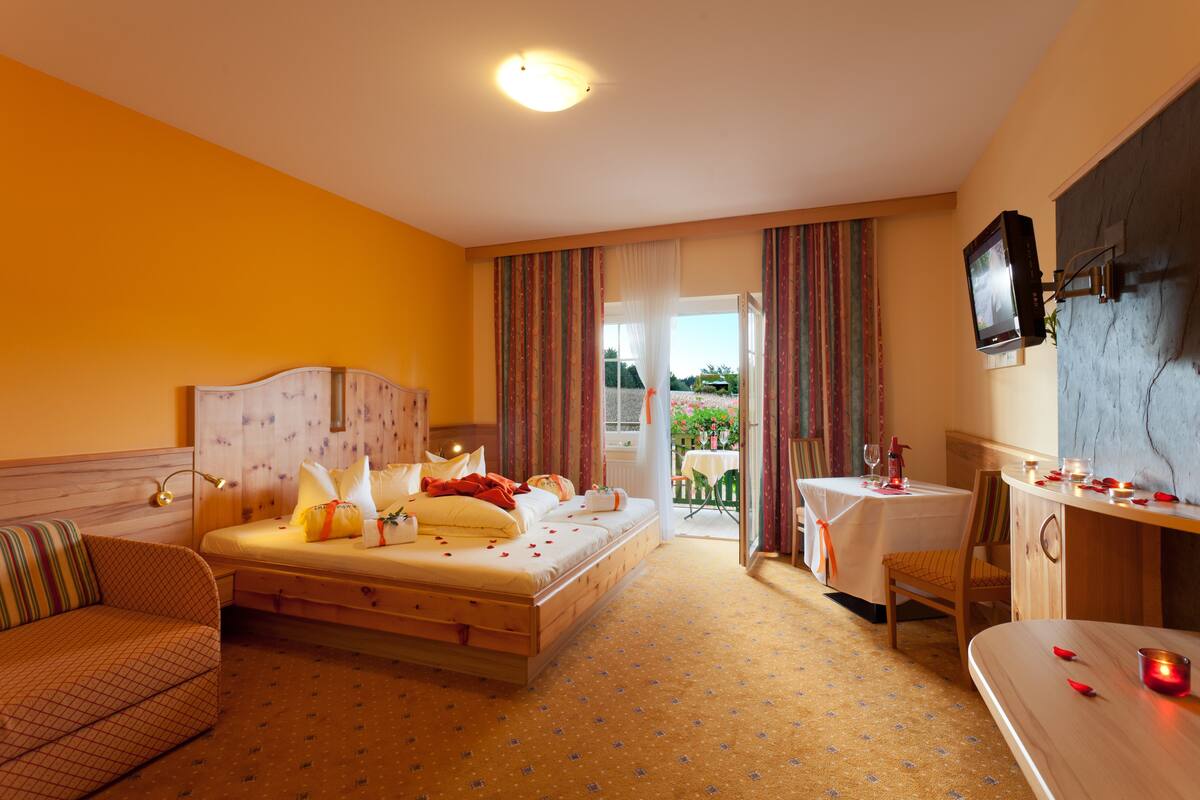 A hotel room with a bed, a sofa, a dining table, and a TV mounted on the wall.