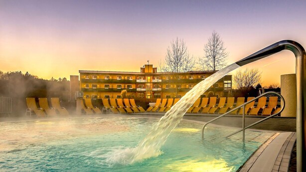 Una piscina con elemento d'acqua, sedie a sdraio gialle e un edificio sullo sfondo.