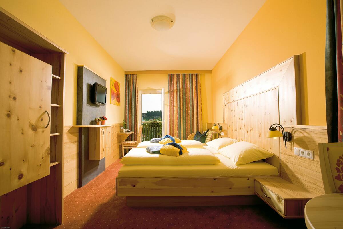 A room with a bed, a television, a window with curtains, and a wooden wardrobe.