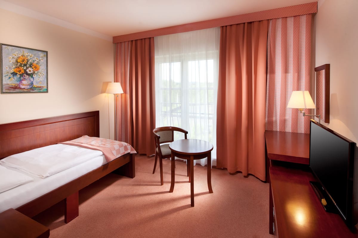 Habitación de hotel con cama, una silla, una mesita, televisor y ventana con cortinas.