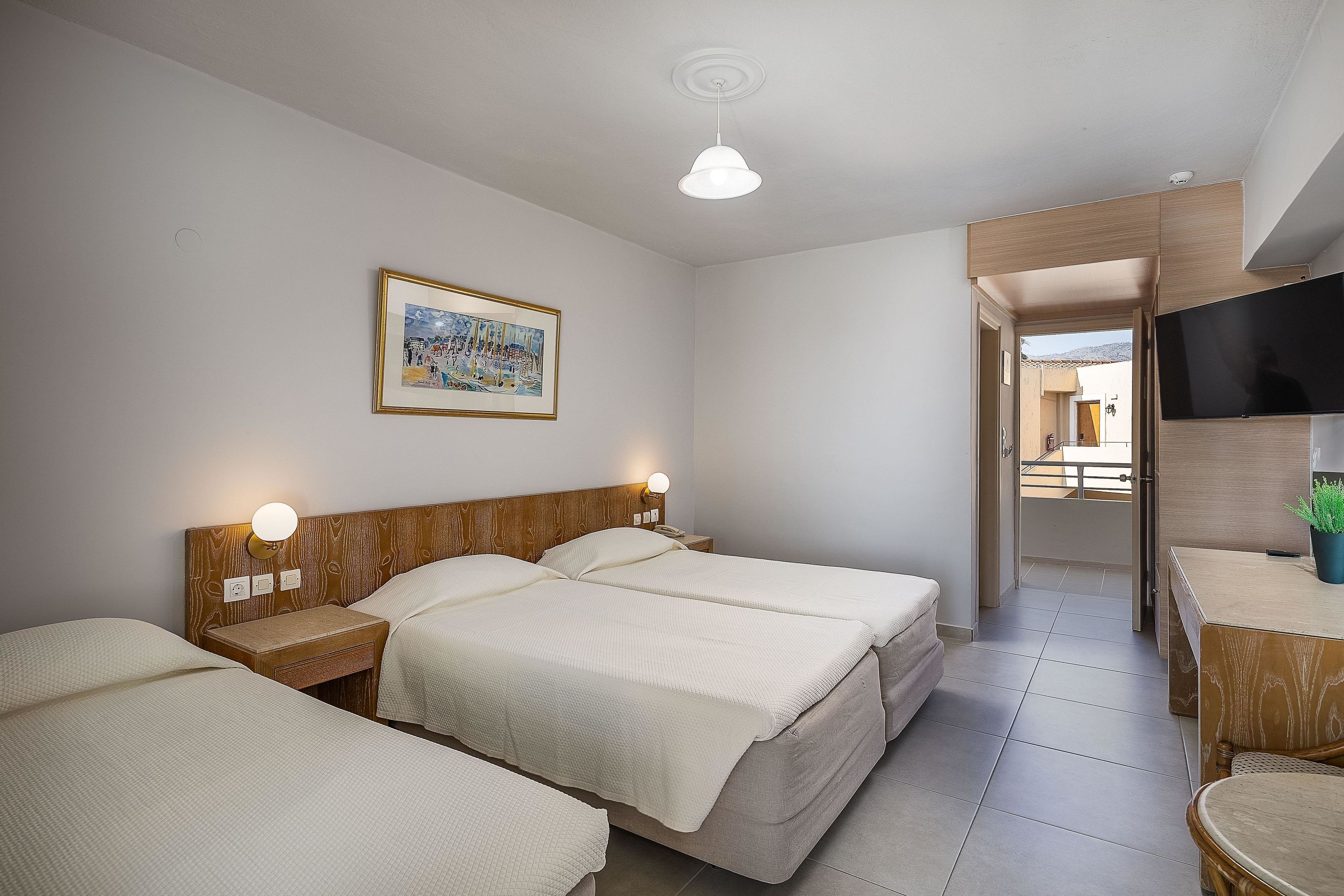 Une chambre d’hôtel avec deux lits, une tête de lit en bois, des lampes de chevet, un téléviseur à écran plat et un tableau encadré au mur.