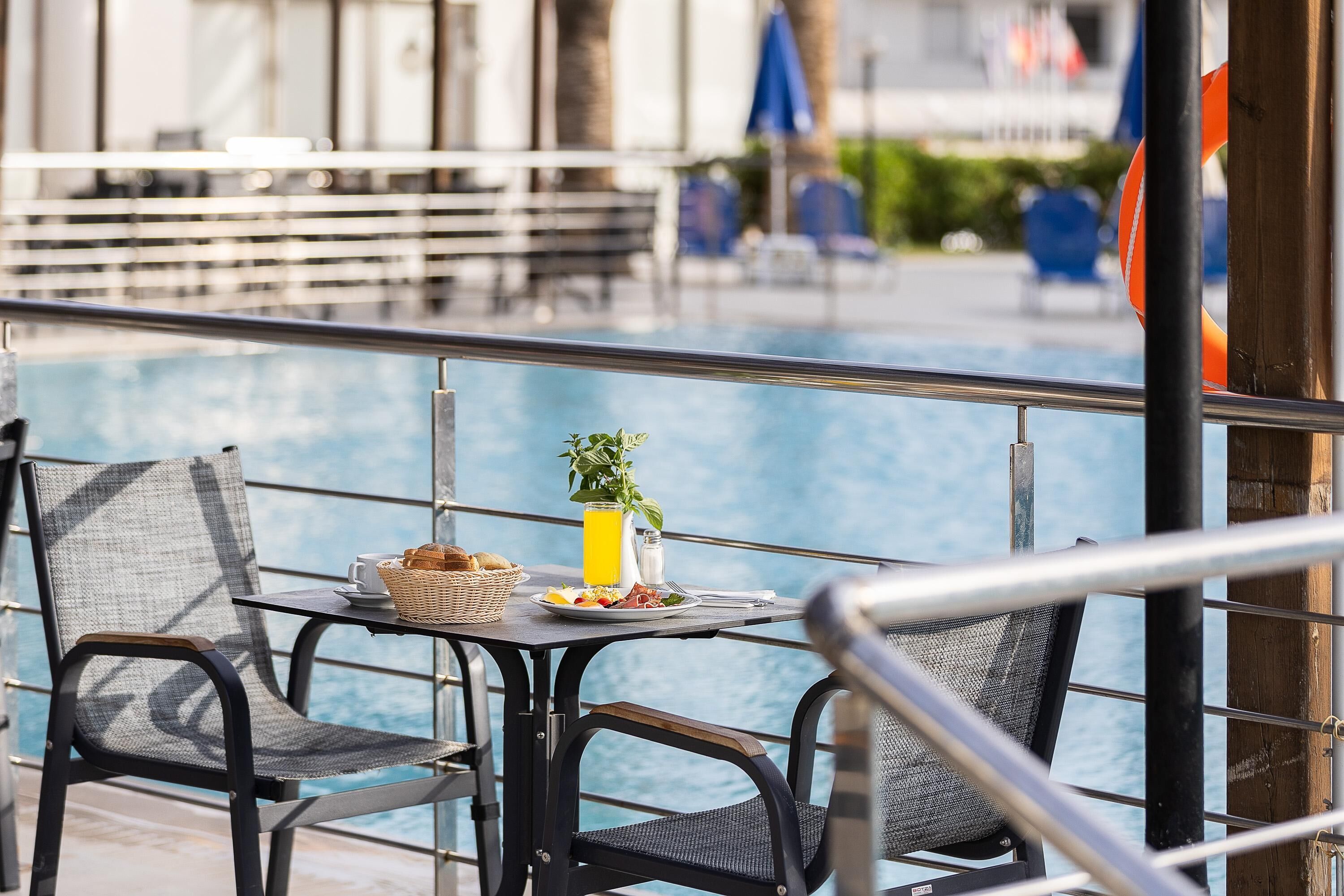 Ein Tisch am Pool mit einem Korb, einem Glas Orangensaft und einem Teller Essen.