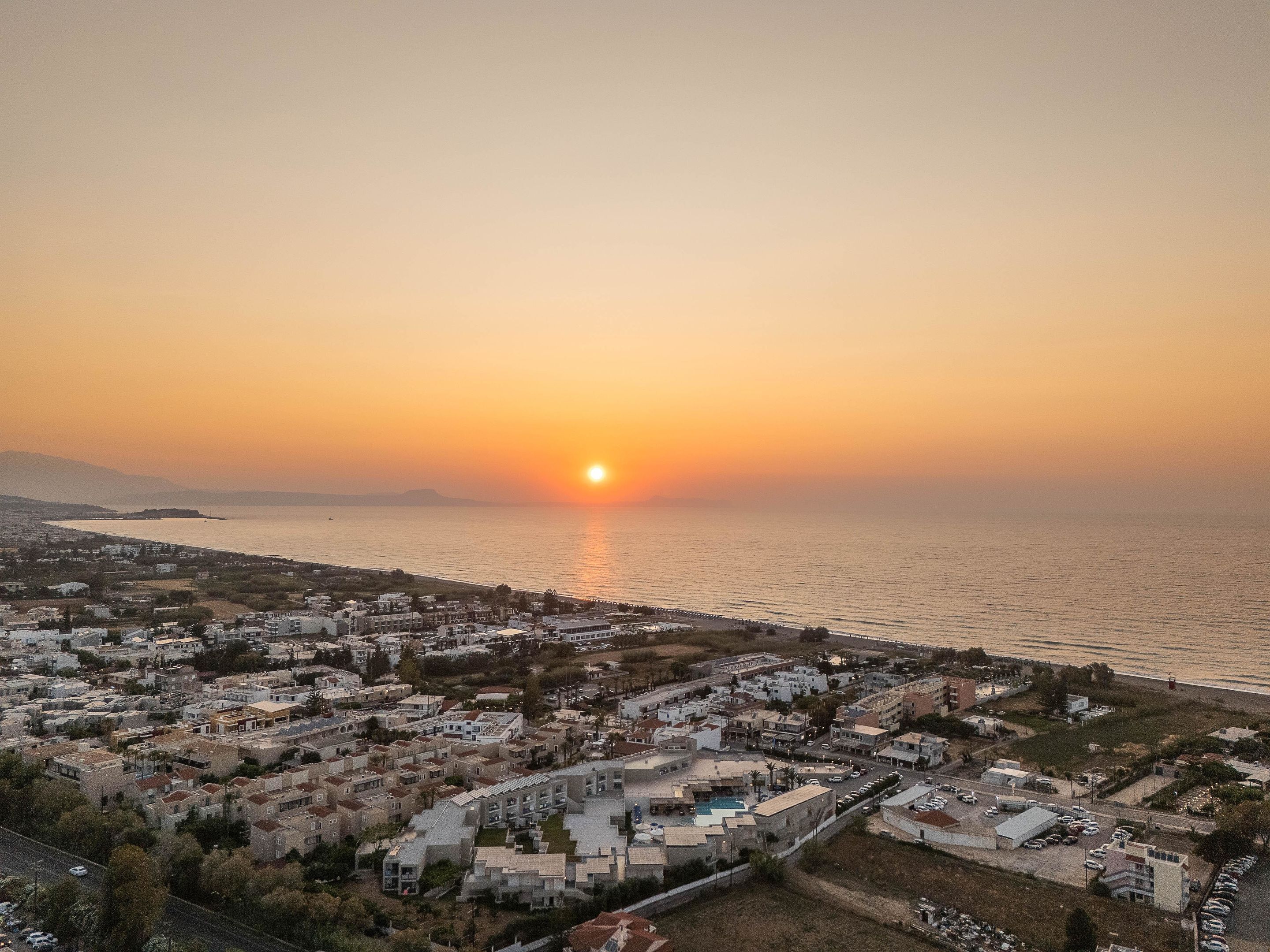 Un pueblo costero al atardecer, con edificios a lo largo del paseo marítimo y una vista despejada del mar.
