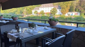 An outdoor dining area with wicker furniture, a table set with white tableware, and potted plants. - Hotel Victoria (Bad Kreuznach)