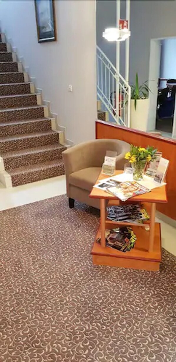 A carpeted area with a chair and a small table with magazines and a vase of flowers. - Hotel Victoria (Bad Kreuznach)