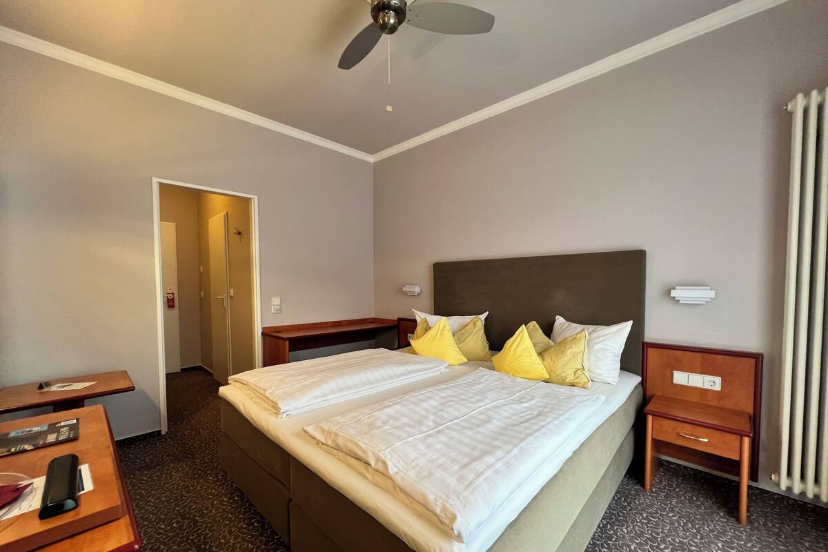 A hotel room with a bed, bedside tables, a desk, and a ceiling fan.