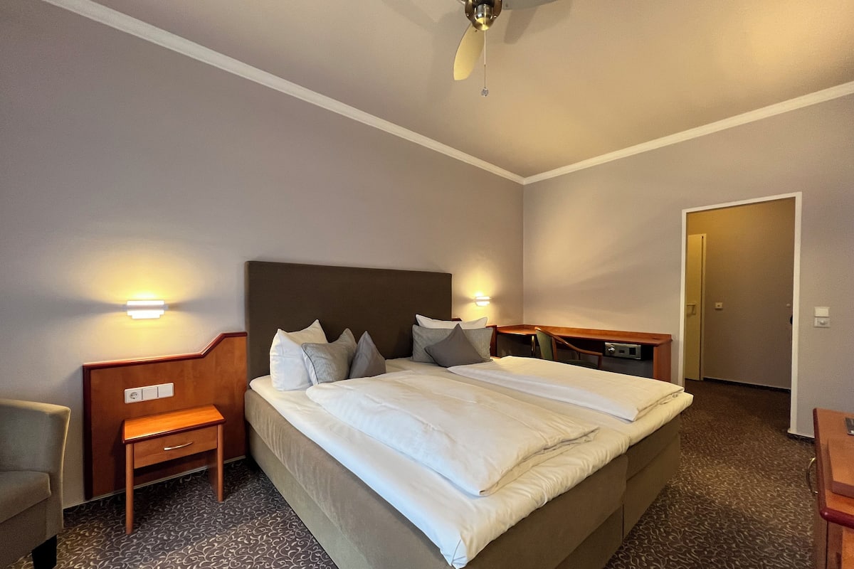 A hotel room with a large bed, bedside tables, a chair, and a desk.